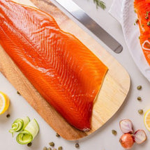 Raw salmon fillet on a wooden board with garnished salmon dish and lemon slices on a light background.