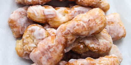 A batch of glazed Yum Yum doughnuts on a white surface.