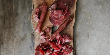 Wooden board with various cured meats on a concrete surface